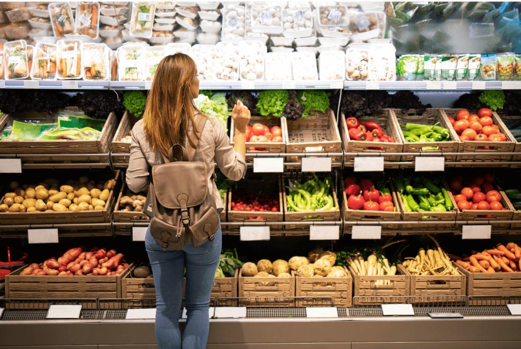 Woman shopping in a supermarket, looking at plant-based nutritious foods like fruits and vegetables