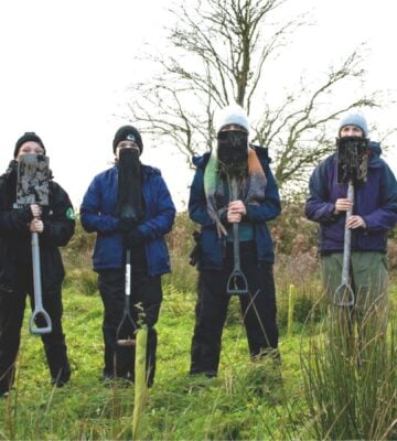 Members of the Vegan Land Movement standing in a field holding spades that cover their faces