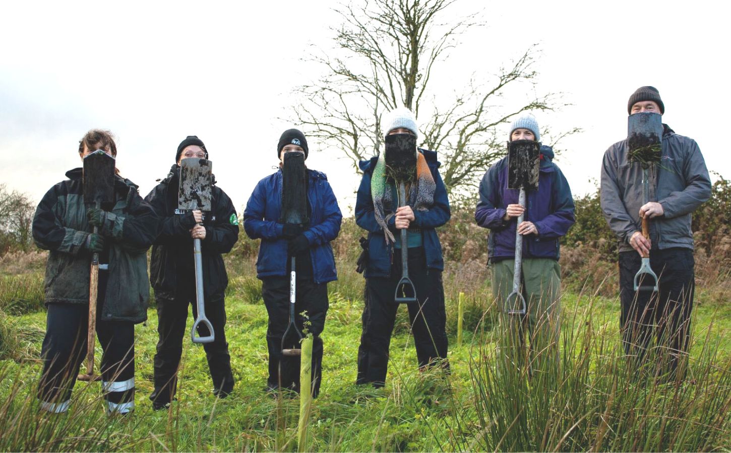 Members of the Vegan Land Movement standing in a field holding spades that cover their faces