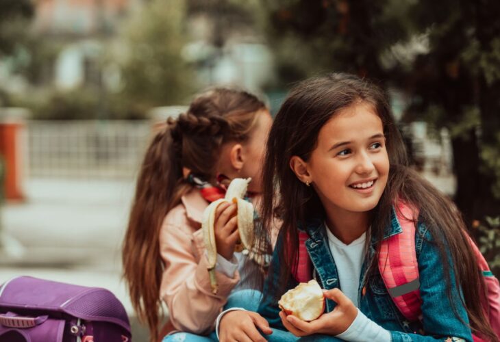 Children eating healthy plant-based food like fruit at a school
