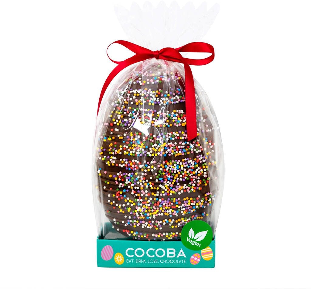 A Cocoba vegan dark chocolate Easter egg with colourful sprinkles, wrapped in cellophane and tied with a red bow