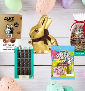 A range of vegan and dairy-free Easter chocolate and candy on a wooden plank backdrop, flanked by pastel Easter eggs
