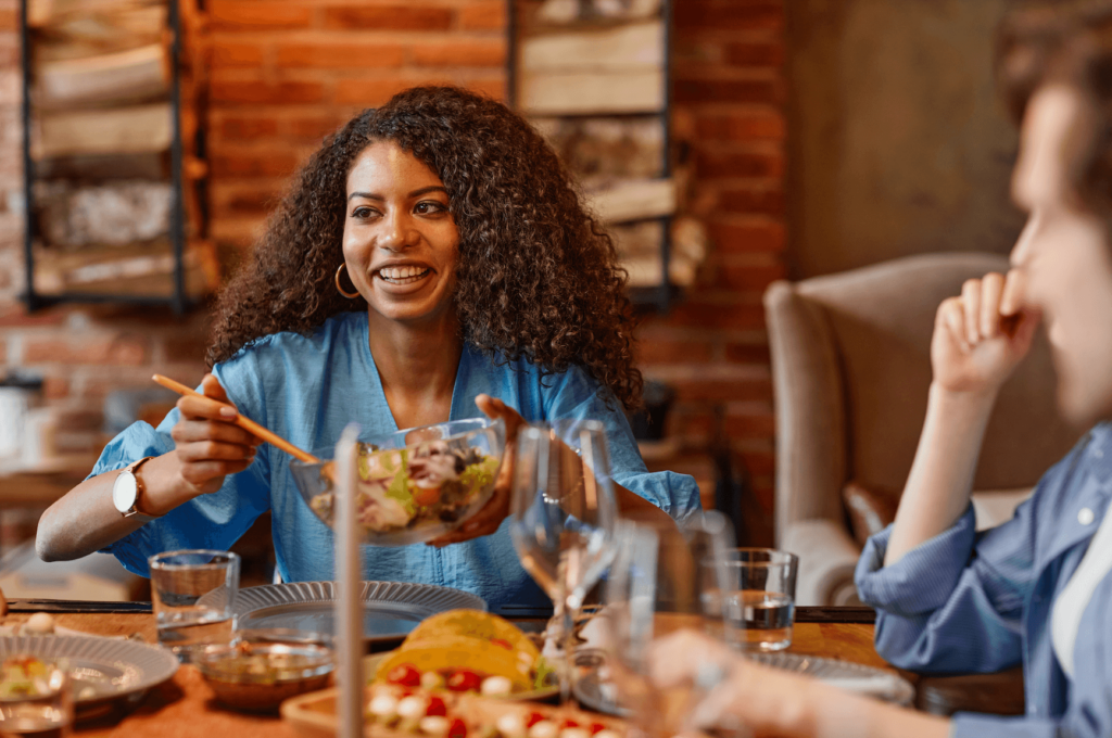 A woman eating plant-based food with friends at a dinner table
