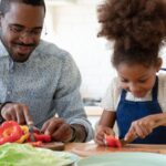 A child and her father cutting vegan food like peppers in the kitchen