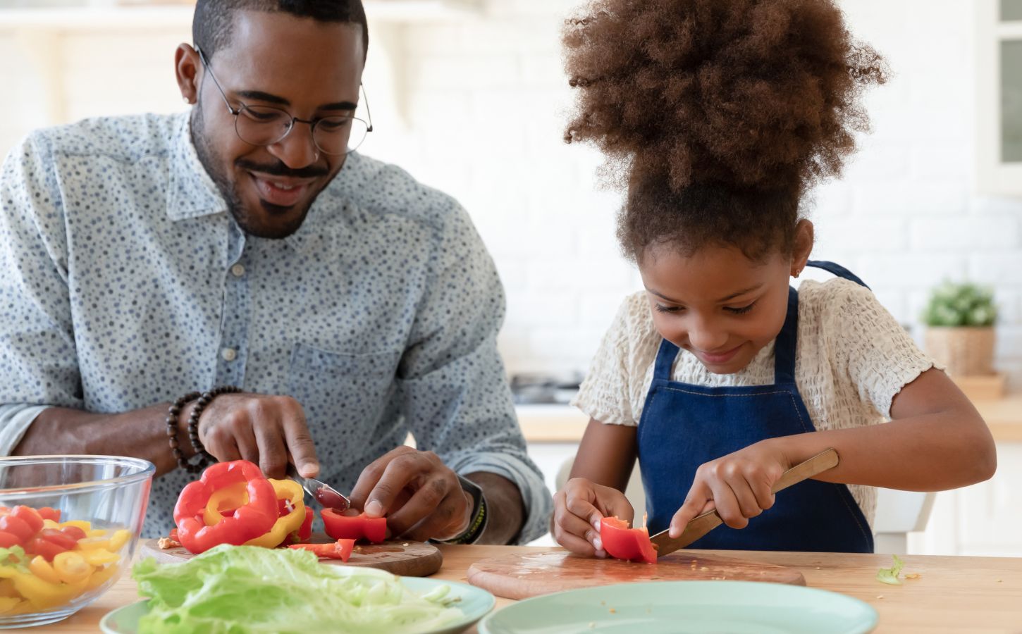 A child and her father cutting vegan food like peppers in the kitchen