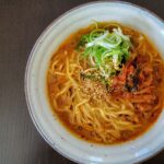 Freshly prepared vegan kimchi miso ramen in a white stoneware bowl, on a dark table