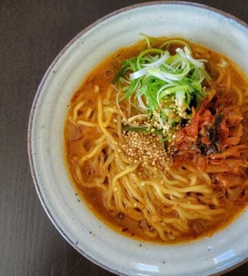 Freshly prepared vegan kimchi miso ramen in a white stoneware bowl, on a dark table