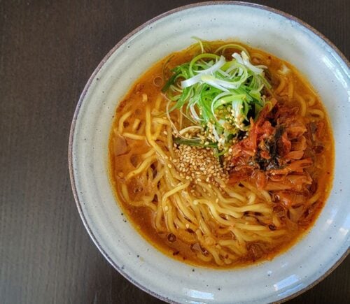 Freshly prepared vegan kimchi miso ramen in a white stoneware bowl, on a dark table