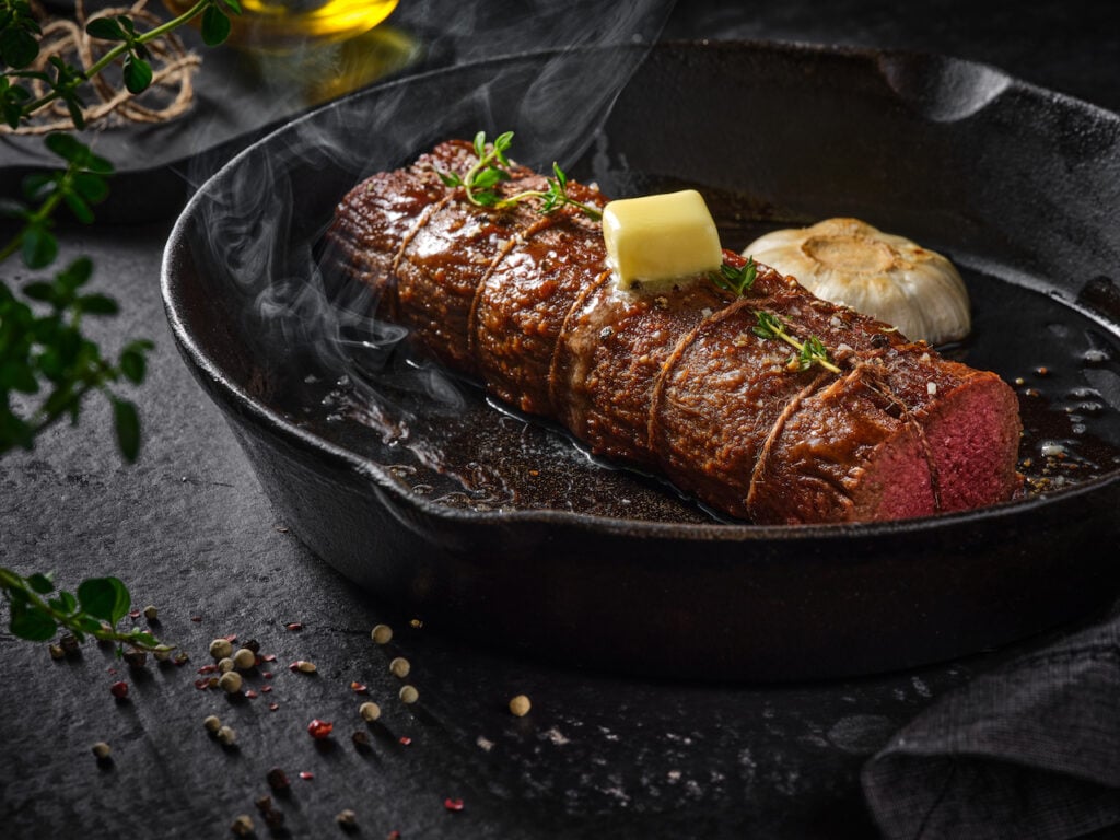 A vegan tenderloin steak searing in a hot pan with a knob of plant-based butter on top