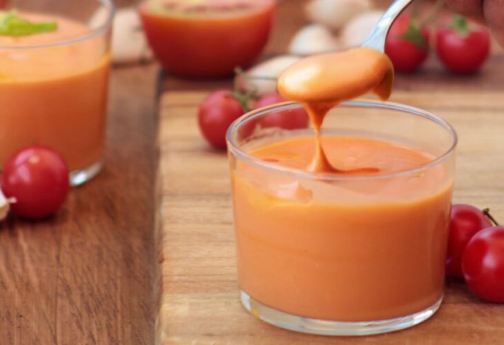 Glasses of vegan salmojero, with a spoon dipping in, surrounded by cherry tomatoes