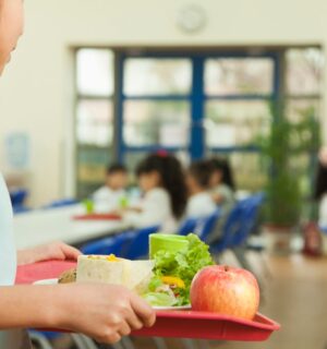 A young student for somewhere to sit in a school cafeteria in Taiwan, holding a tray with plant-based food
