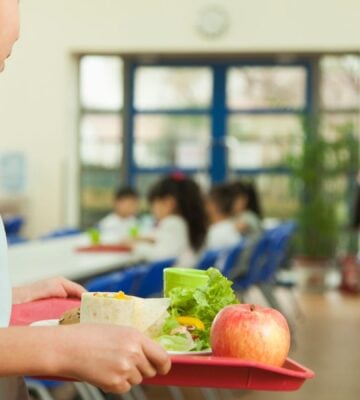A young student for somewhere to sit in a school cafeteria in Taiwan, holding a tray with plant-based food