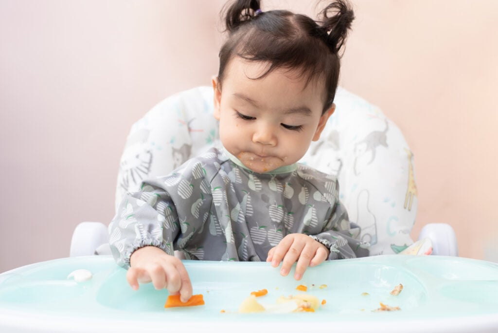 A baby in a child's high chair eating vegan food