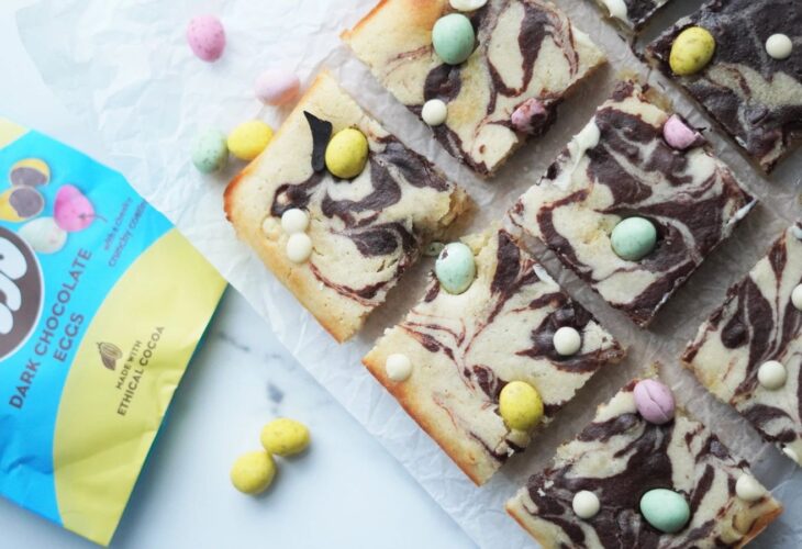 Vegan easter blondie bites laid out on a marble work surface, surrounded by vegan chocolate mini eggs