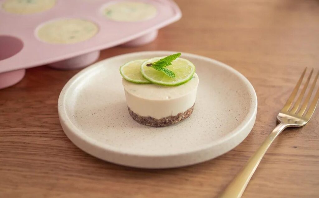 An individual dairy-free and vegan mojito cheesecake on a natural stone plate with a gold fork next to it