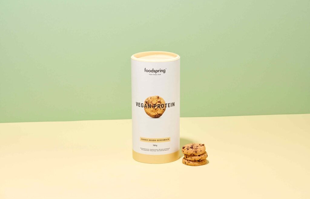 A tube of Foodspring vegan protein powder in front of a green background