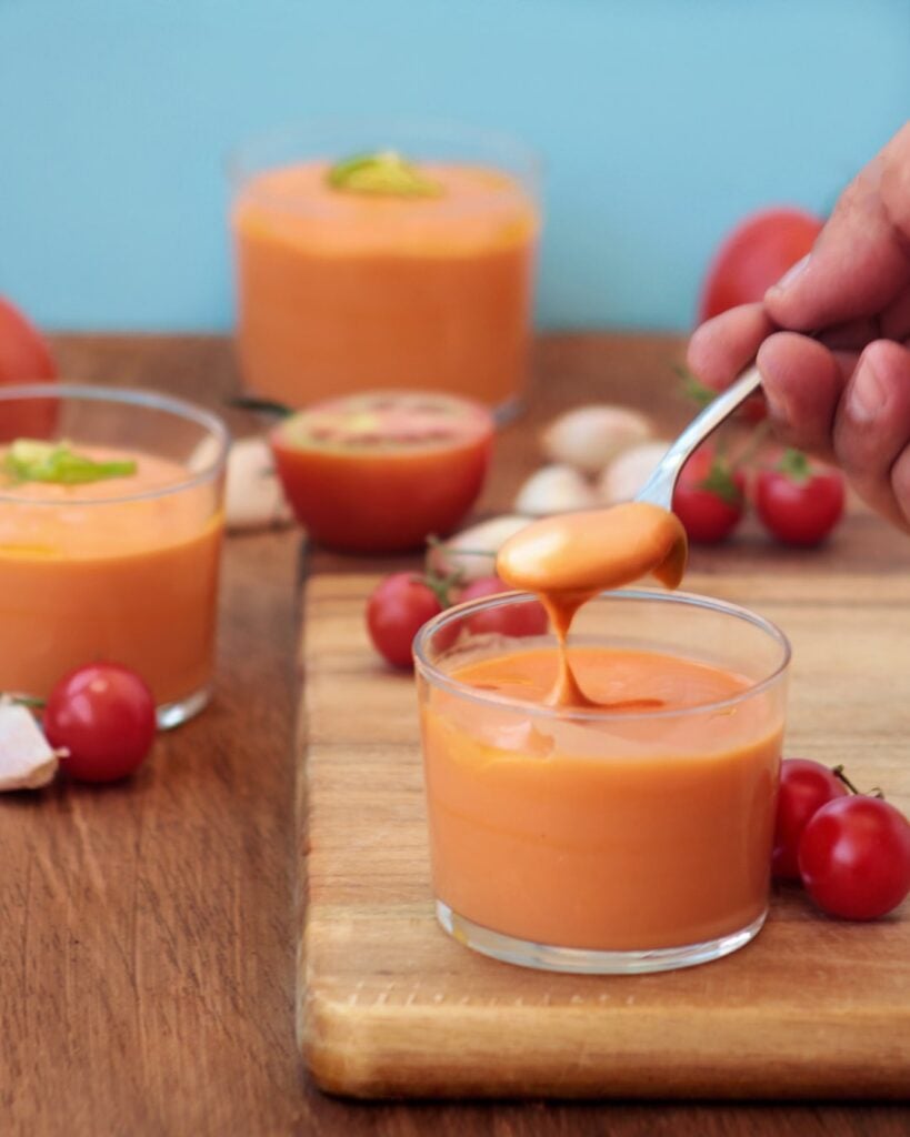 Glasses of vegan salmojero, with a spoon dipping in, surrounded by cherry tomatoes