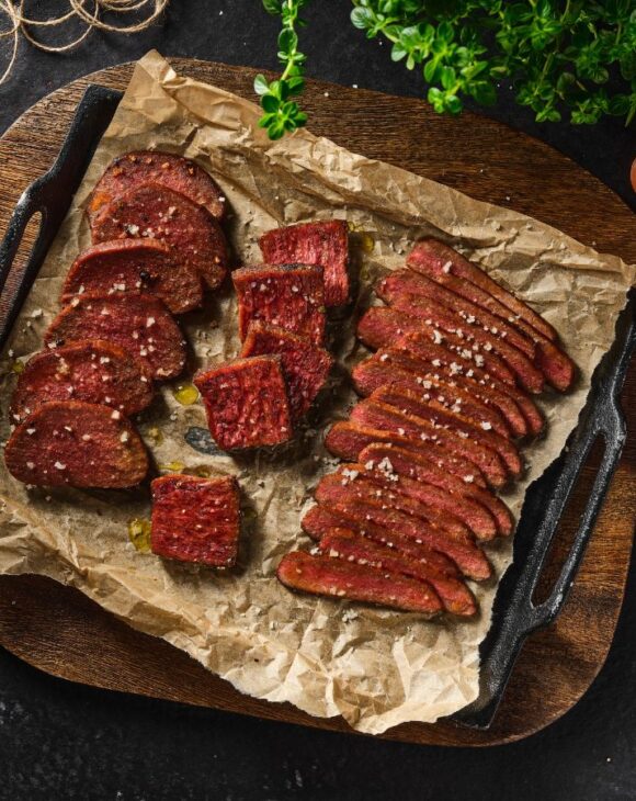 A selection of vegan steak cuts on a griddle tray, surrounded by onions and other ingredients
