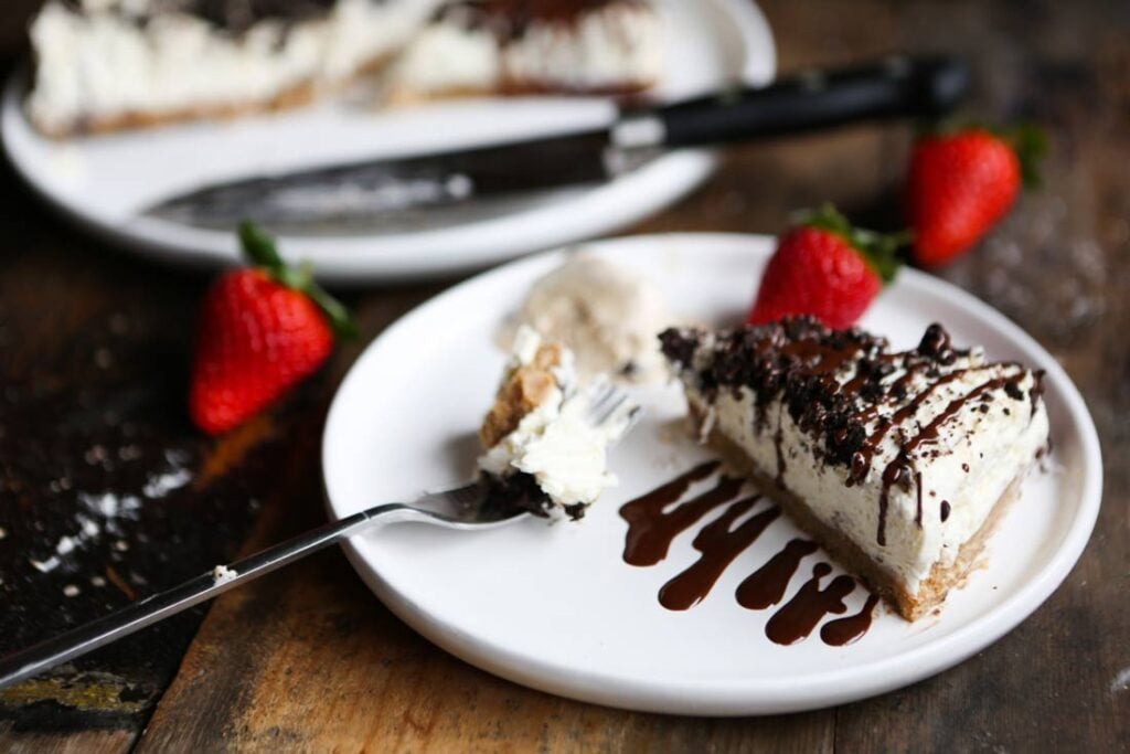 A vegan vanilla Oreo cheesecake on a plate, served with chocolate sauce and ice cream