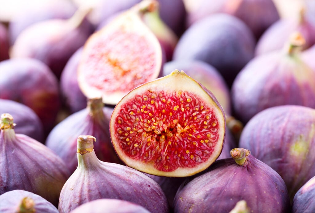 A cut open vegan-friendly fig sitting on top of some whole ones