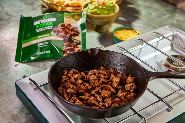 Beyond Steak being fried in a frying pan with the green product packaging in the background