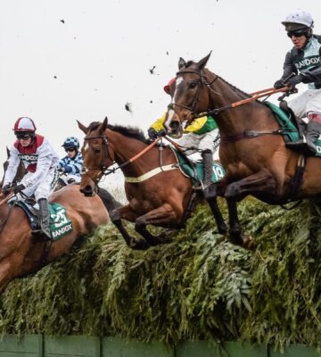 Three horses and jockeys jumping over a fence during a horse race at the Aintree Grand National