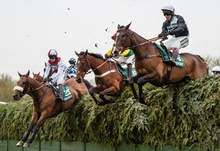 Three horses and jockeys jumping over a fence during a horse race at the Aintree Grand National