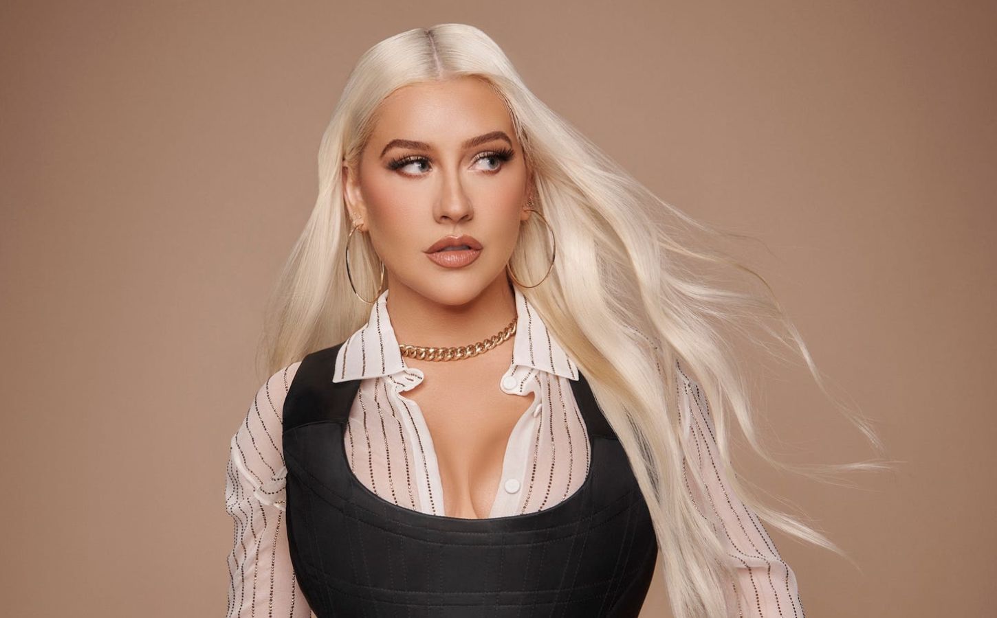 Christina Aguilera standing in front of a neutral background wearing a white shirt and black corset top with long straight blonde hair