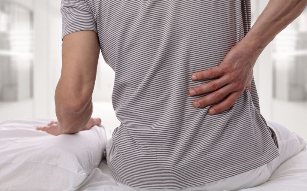A man sat on a bed clutching his back in pain