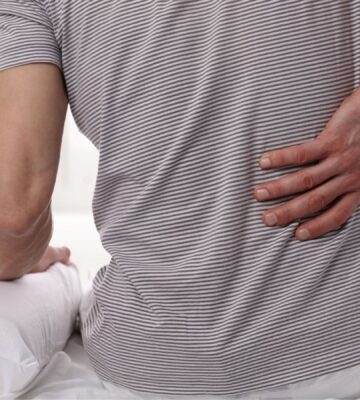 A man sat on a bed clutching his back in pain
