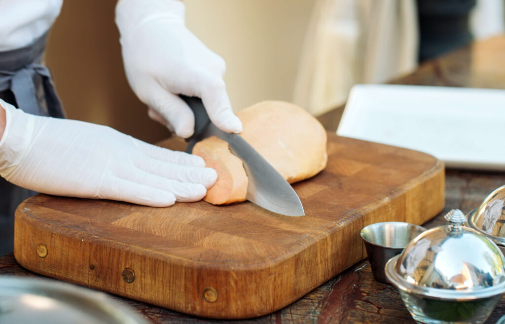 An engorged bird liver being sliced by a chef to serve as a foie gras dish