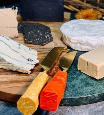A selection of vegan dairy-free cheeses from la Fauxmagerie on a wooden and resin board with appropriate knives