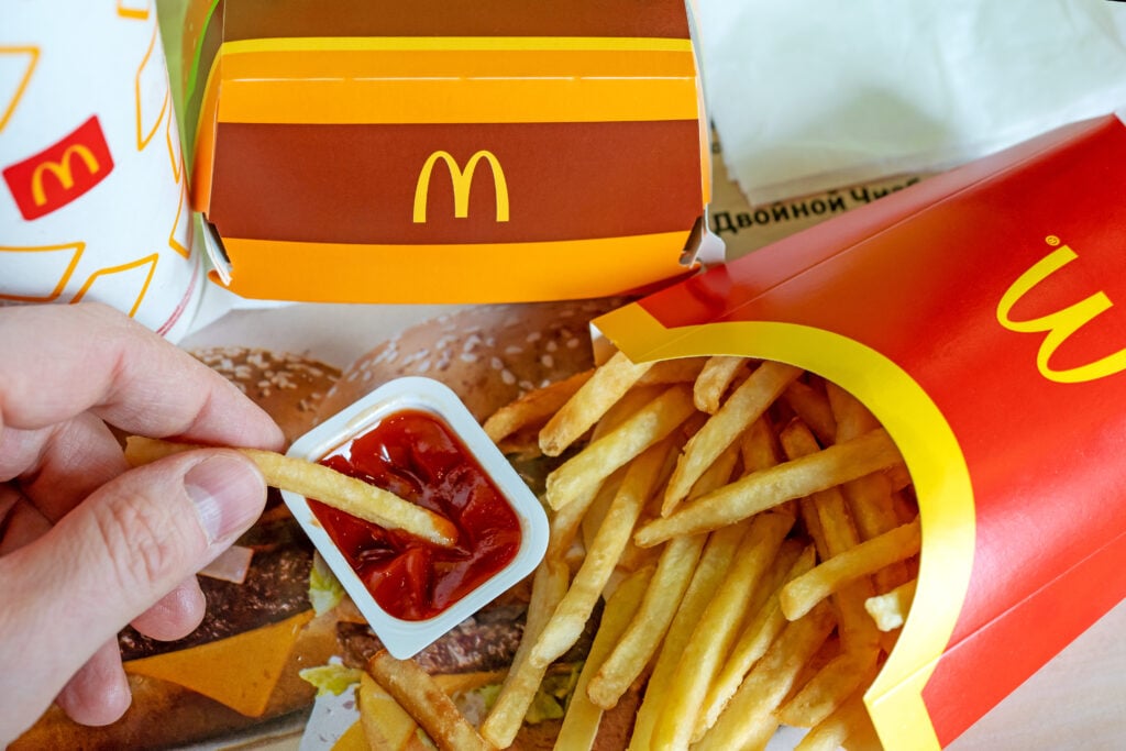 A person eating vegan-friendly McDonald's fries and dipping a chip in Ketchup