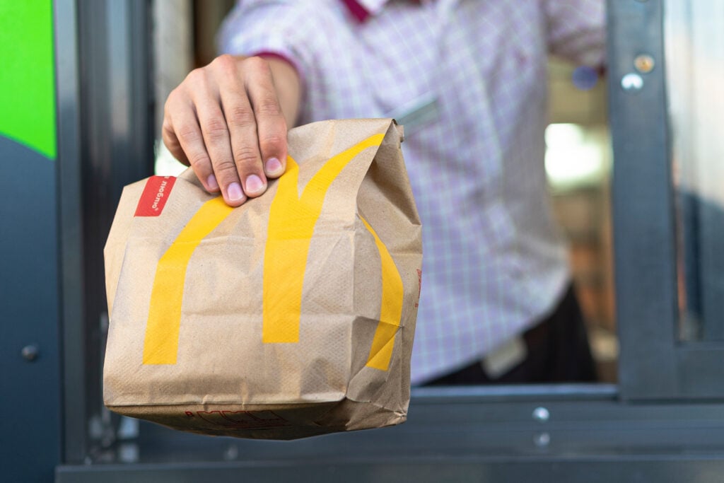 A Mcdonald's worker handing out a bag in a Drive Thru