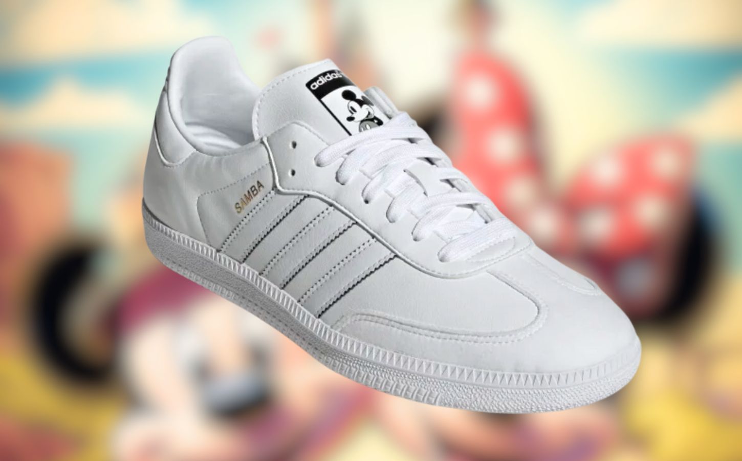 All-white vegan Adidas x Disney Samba sneakers with Mickey Mouse motifs, with a blurred image of Mickey and Minnie in the background