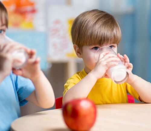 Two children drink milk and eat apples
