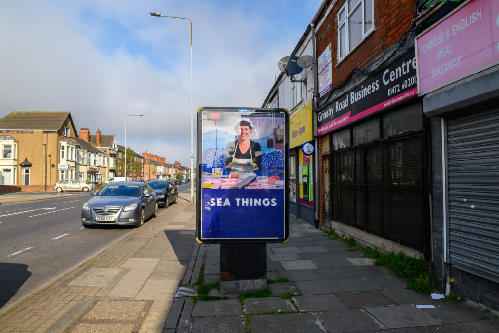 A PETA billboard showing a smiling fishmonger holding a dead fish, which turns into a dead cat