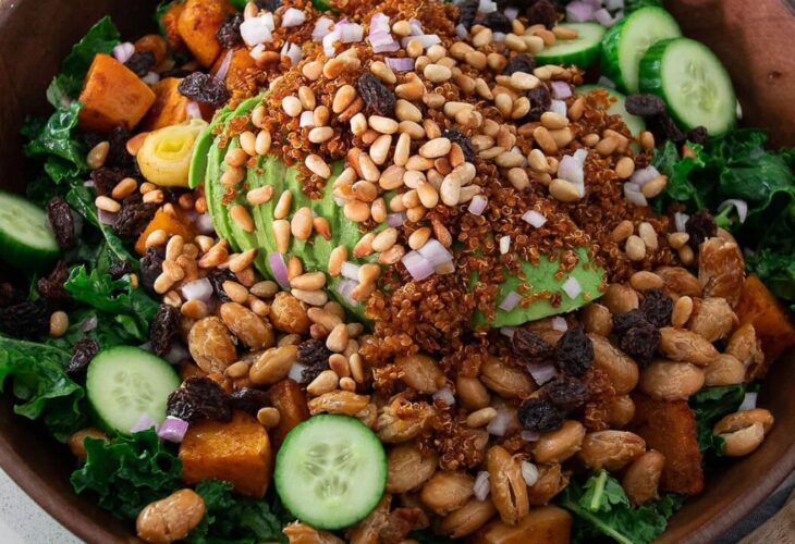 Warm pumpkin and kale vegan salad served in a large ceramic bowl, on a scenic recipe table with dressing on the side