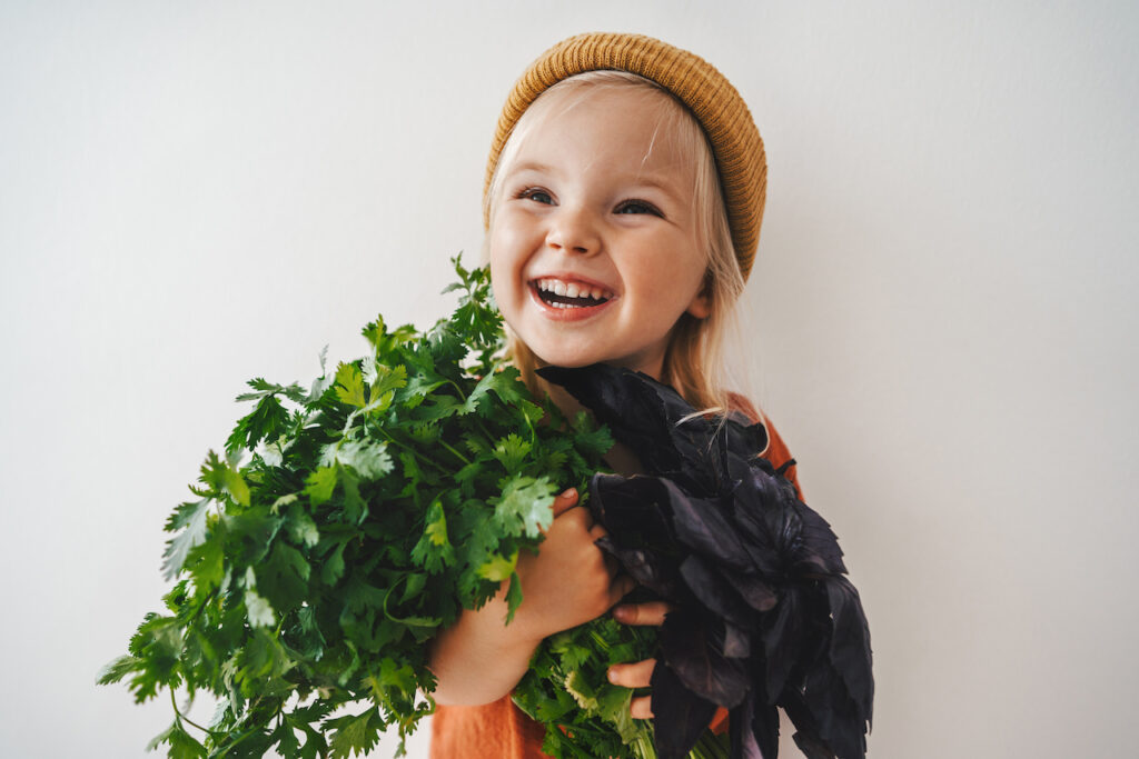 A smiling child holding bunches of coriander and basil