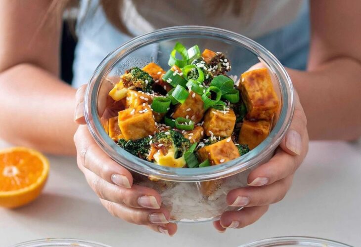 bowls of freshly prepared orange tofu and broccoli, one being held by the recipe developer from Plant Baes