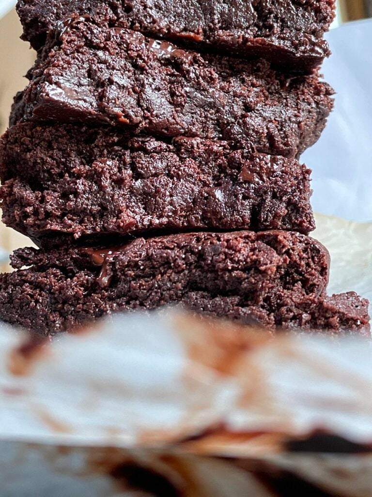 A stack of freshly cut vegan flourless tahini chocolate brownies on parchment paper