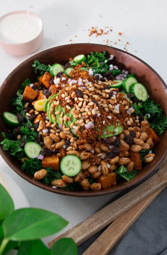Warm pumpkin and kale vegan salad served in a large ceramic bowl, on a scenic recipe table with dressing on the side