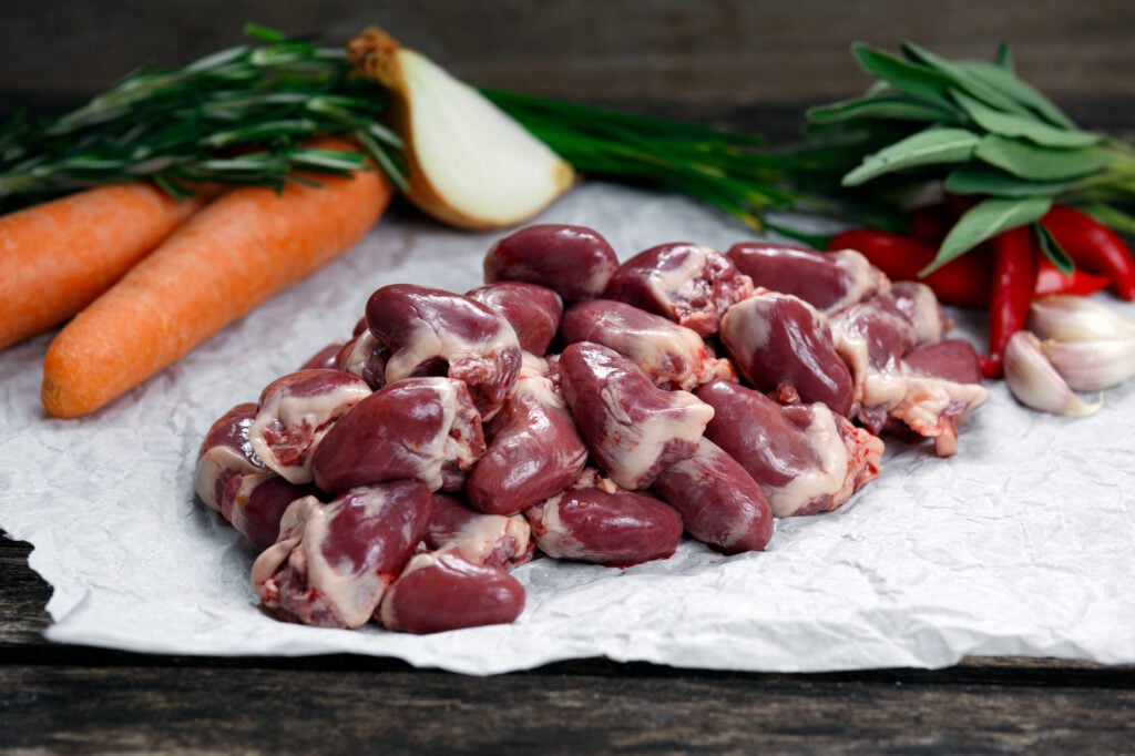Organ meat (Raw duck hearts) lying on a table next to some vegetables