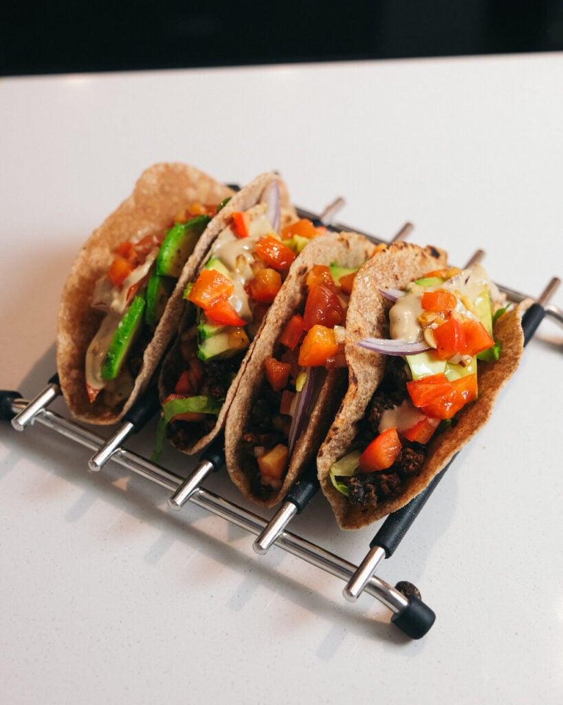 Vegan tacos sat in a rack, filled with fresh filling, salsa and toppings