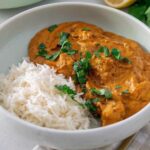 A white bowl full of vegan butter chicken curry and rice with a fresh coriander garnish