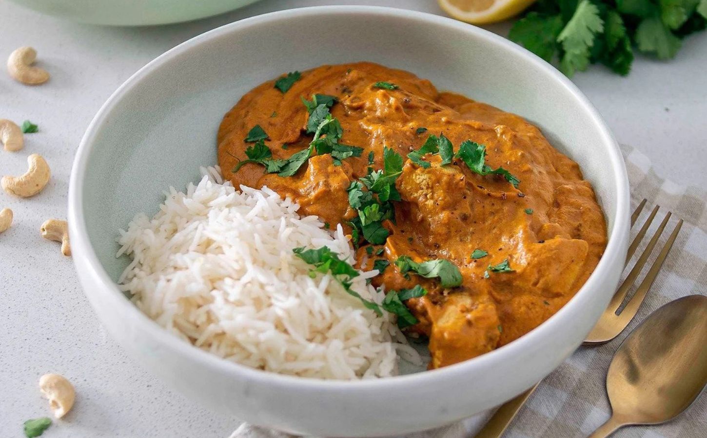 A white bowl full of vegan butter chicken curry and rice with a fresh coriander garnish