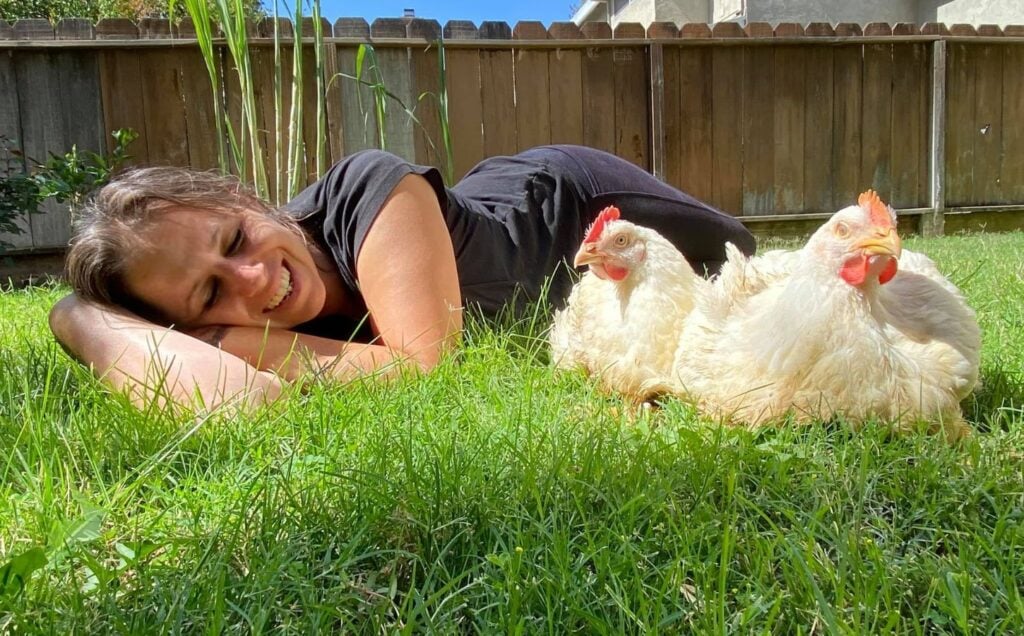 Direct Action Everywhere activist Alicia Santurio lying on the grass with two rescued chickens