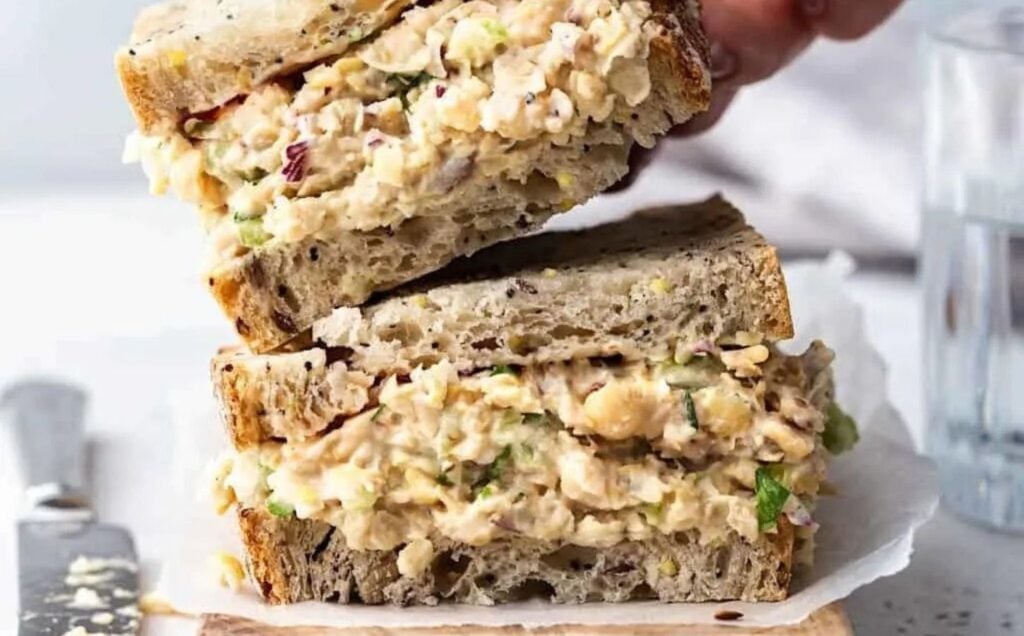 A vegan chickpea tuna mayo sandwich being placed on a wooden board