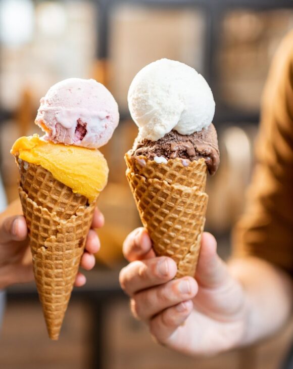 Hands holding two ice cream cones containing scoops of dairy-free ice cream