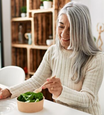 An older woman eating a bowl of green lettuce